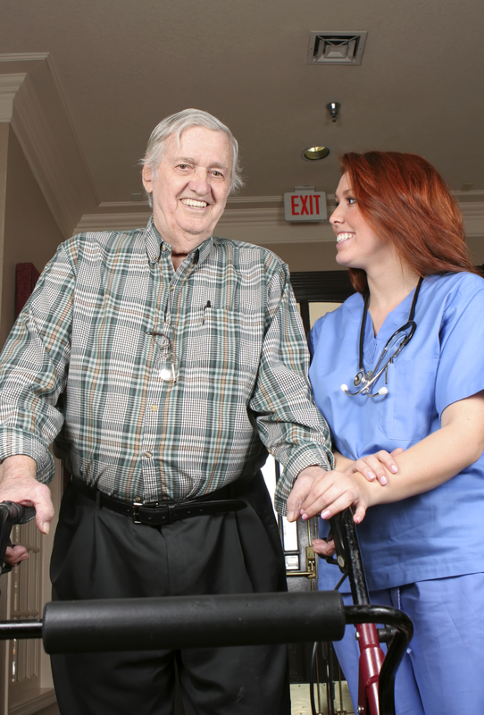Elderly man with nurse using walker indoors.