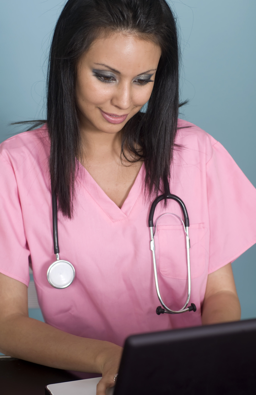 Nurse in pink scrubs using laptop.