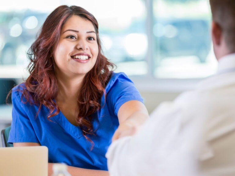 Smiling woman in blue scrubs, handshake.