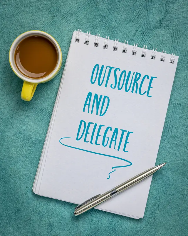 Notebook, pen, coffee cup, "Outsource and Delegate".