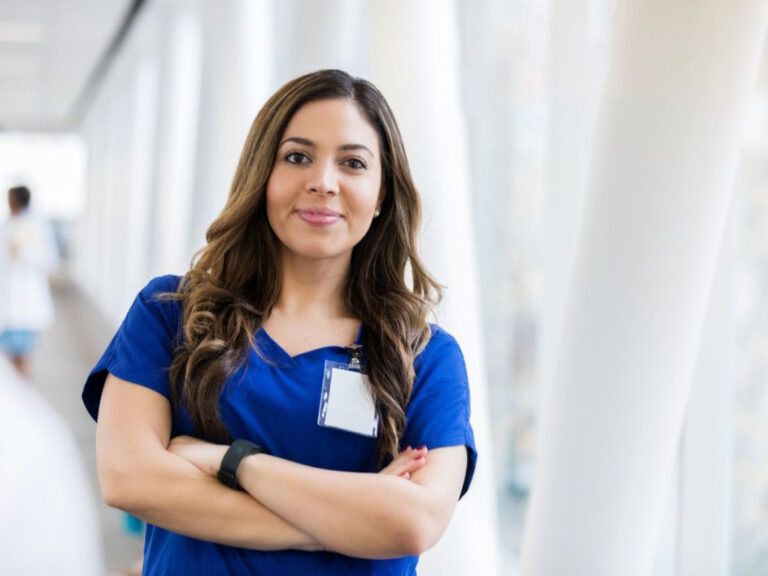 Smiling woman in blue scrubs, arms crossed.